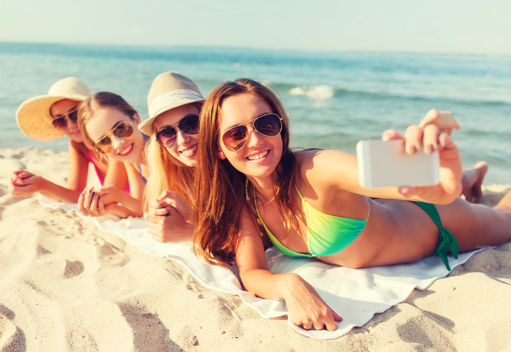 Ragazze sorridenti con smartphone sulla spiaggia