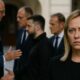 Giorgia Meloni in primo piano con espressione seria; sullo sfondo sfocato i leader europei dialogano tra loro, senza di lei.