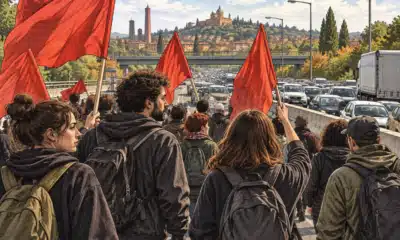 Manifestanti su una carreggiata chiusa al traffico, con auto ferme in coda sullo sfondo.