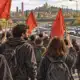 Manifestanti su una carreggiata chiusa al traffico, con auto ferme in coda sullo sfondo.