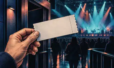 Una mano anonima tiene un biglietto senza scritte davanti a una sala da concerto illuminata.