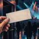 Una mano anonima tiene un biglietto senza scritte davanti a una sala da concerto illuminata.