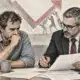 Un piccolo imprenditore e un consulente esaminano insieme documenti non leggibili in un ambiente di lavoro sobrio.
