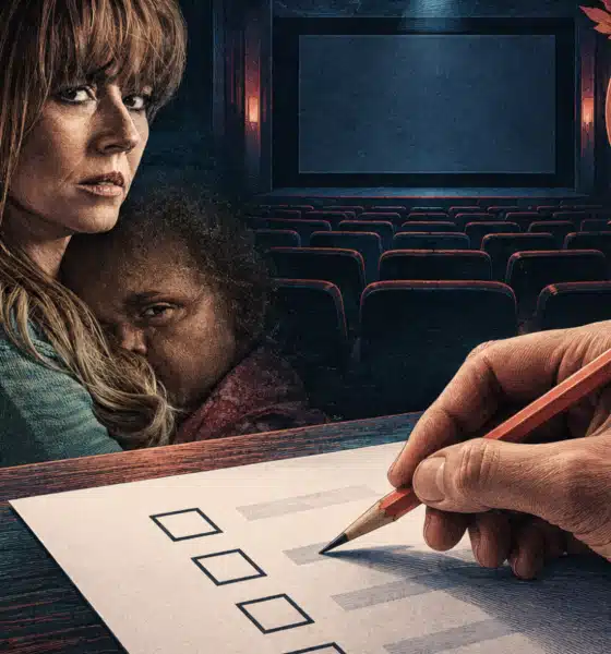 Una mano anonima tiene una matita sopra una scheda bianca, davanti a uno schermo cinematografico spento.