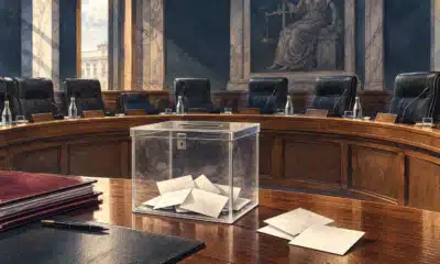 Illustrazione di un tavolo istituzionale con un’urna chiusa e schede anonime, in una sala consiliare sobria.