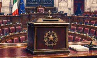 Un’urna per il voto parlamentare in primo piano, con l’aula di Montecitorio sullo sfondo.