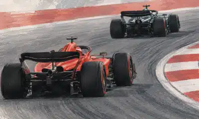 Illustrazione di una monoposto Ferrari rossa che segue una Mercedes scura in pista.
