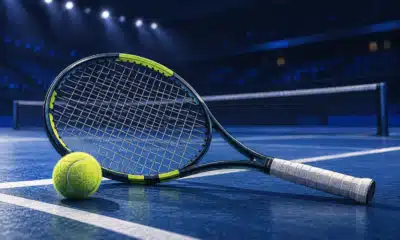 Una racchetta da tennis in primo piano davanti a un campo indoor vuoto, in un’illustrazione sul ritiro di Arthur Fils.