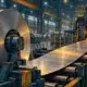 Illustrazione di una linea siderurgica con nastri d’acciaio e macchinari in un impianto industriale.