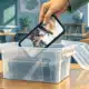 Una mano ripone uno smartphone in un contenitore su un banco, in un’aula scolastica.