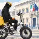 Illustrazione di un rider con casco fermo sulla bicicletta da consegna in una strada urbana essenziale.