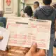 Un foglio di prenotazione sanitaria in primo piano e alcune figure in una sala d’attesa stilizzata.