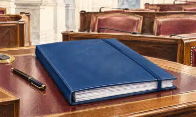 Un fascicolo chiuso su un banco parlamentare, con sedute vuote sullo sfondo.
