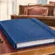 Un fascicolo chiuso su un banco parlamentare, con sedute vuote sullo sfondo.