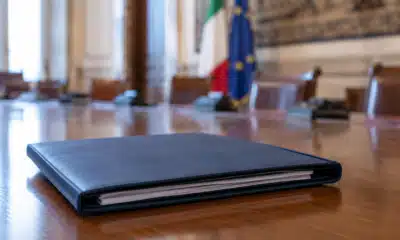 Un fascicolo di bilancio chiuso su un tavolo istituzionale, con una sala riunioni sullo sfondo