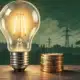Illustrazione di una lampadina accesa accanto a una piccola pila di monete, a evocare il tema del prezzo dell’elettricità.