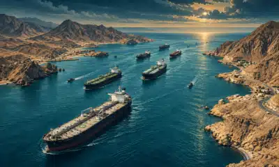 Petroliera e navi mercantili attraversano uno stretto tra coste rocciose.