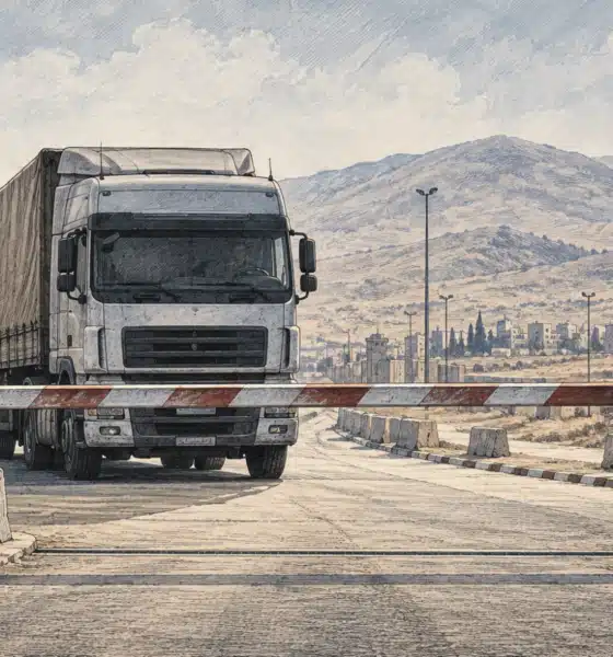 Una barriera abbassata blocca un camion davanti a un valico di frontiera vuoto.