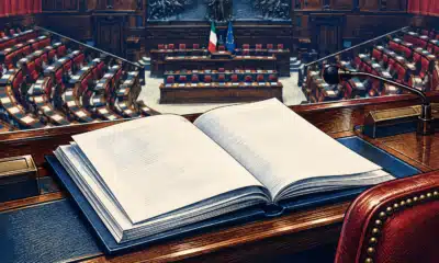 Un fascicolo legislativo aperto su un banco, con l’aula parlamentare sullo sfondo illustrato.