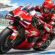 Illustrazione di un pilota in tuta rossa che affronta una curva in sella alla moto da corsa, ispirata alla foto di riferimento.