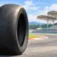 Illustrazione di uno pneumatico slick posteriore da moto da gara, senza marchi, con il tracciato di Sepang appena accennato sullo sfondo.