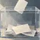 Illustrazione di un’urna elettorale trasparente con alcune schede al suo interno.