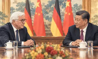 Illustrazione editoriale di due presidenti seduti a un tavolo diplomatico, con i drappi tedeschi e cinesi sullo sfondo.