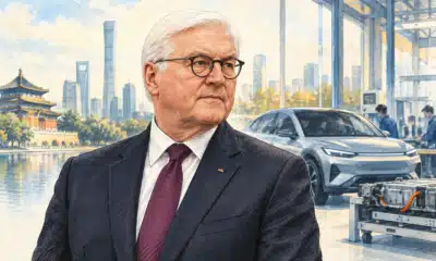Ritratto illustrato di Frank-Walter Steinmeier davanti a un ambiente simbolico di ricerca automobilistica, con una sagoma di veicolo elettrico sullo sfondo.