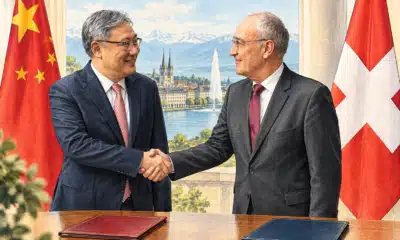 Illustrazione editoriale di due uomini ispirati ai soggetti della foto di riferimento che si stringono la mano, con le bandiere svizzera e cinese sullo sfondo e una cartella chiusa in primo piano.