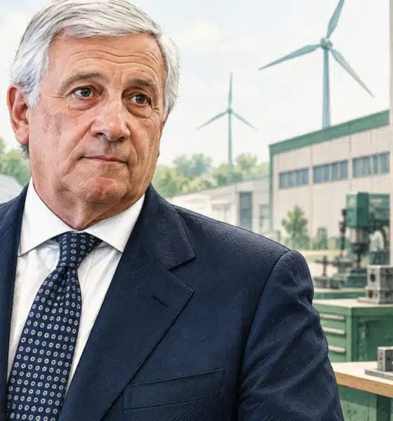 Ritratto illustrato di Tajani davanti a un piccolo ambiente produttivo con un quadro elettrico sullo sfondo.