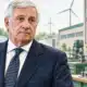 Ritratto illustrato di Tajani davanti a un piccolo ambiente produttivo con un quadro elettrico sullo sfondo.