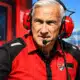 Ritratto illustrato di un dirigente Ducati in tuta rossa e nera, su uno sfondo essenziale ispirato a un box di MotoGP.