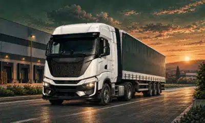 Illustrazione di un camion per il trasporto merci davanti a un contesto industriale essenziale.