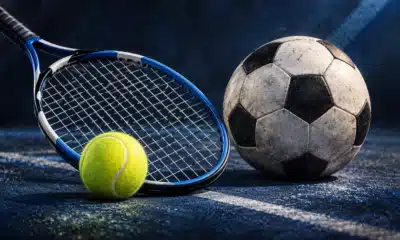 Una racchetta da tennis e una palla da calcio accostate su uno sfondo blu scuro.