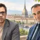 Due uomini raffigurati in ritratti editoriali separati, con un dettaglio di Torino sullo sfondo luminoso.