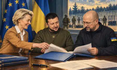 Fascicolo blu e registro aperto su un tavolo istituzionale, con un’attività di addestramento appena visibile sullo sfondo.