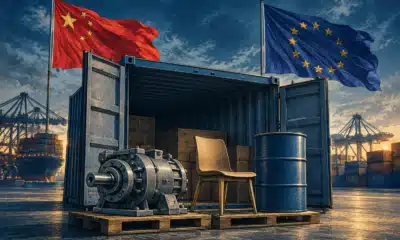 Un container con un componente di macchinario, una sedia e un fusto chiuso; sullo sfondo le bandiere cinese ed europea.