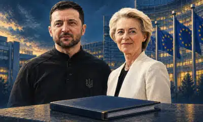 Illustrazione editoriale di Zelensky e von der Leyen accanto a una cartella chiusa, simbolo della proposta di sostegno Ue all’Ucraina ancora in attesa del Consiglio.