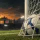Un pallone fermo nella rete di una porta da calcio, illustrato su uno sfondo scuro di campo.