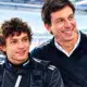 Illustrazione editoriale di Kimi Antonelli in primo piano accanto a Toto Wolff, con un box automobilistico appena accennato sullo sfondo.